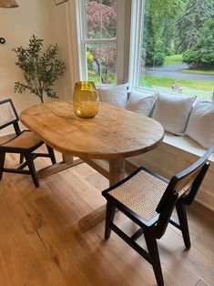 a wooden table sitting in the middle of a living room next to two chairs and a window