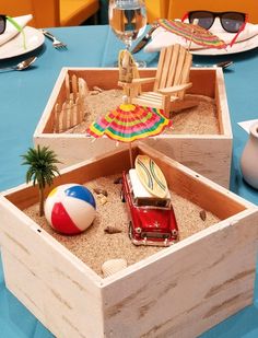 two wooden boxes filled with sand and beach balls on top of a blue table cloth