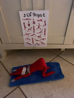 a red stuffed animal laying on top of a blue towel next to a sign that says elf yoga