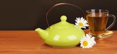 a green teapot next to a cup and saucer with daisies on the side