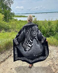 a woman holding up a zebra blanket on top of a dirt road next to a body of water