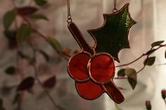 a stained glass ornament hanging from a tree branch with leaves and berries on it