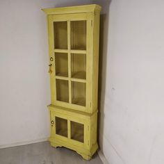 a yellow china cabinet sitting in the corner of a room with a white wall behind it