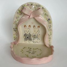 a ceramic figurine with two rabbits on it's side and a pink ribbon around its neck