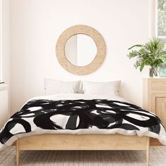 a bed with a black and white comforter next to a round mirror on the wall