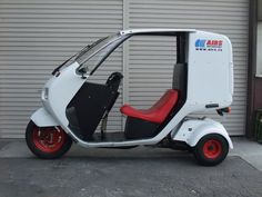 a small white and red scooter parked in front of a garage