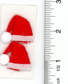 a red and white knitted santa hat next to a measuring ruler on a white surface