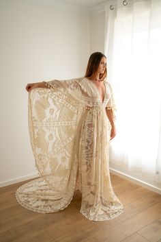 a woman standing in front of a window wearing a white dress and holding a shawl over her shoulders