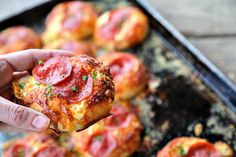 a person holding up a piece of pizza in front of some other small ones on a baking sheet