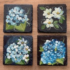 four blue and white flowers painted on black stone coasters, each with different designs