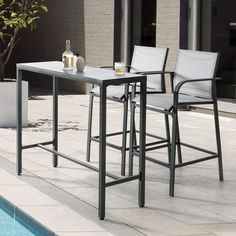 an outdoor table and chairs next to a swimming pool with drinks on the bar stools