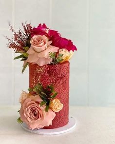 a red and pink cake with flowers on it sitting on a white table next to a wall