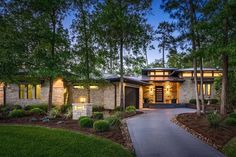 a house with lots of trees and grass in front of it at night, lit up by lights on the windows