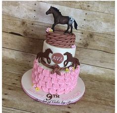 a three tiered cake decorated with pink and brown icing, horse figurines on top