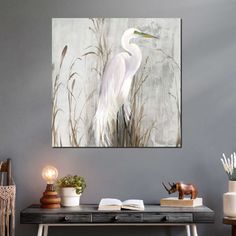 a painting of a white egret on a gray wall above a desk with books