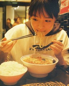 a woman eating noodles with chopsticks at a restaurant