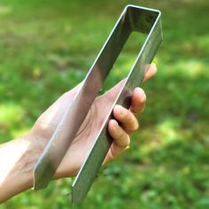 a person holding a metal object in their hand with grass and trees in the background