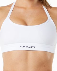 HIGHLIGHTS. Brushed on inside and outside. Smooth and comfortable fabric. Moisture wicking polyester blend. Incredibly stretchy. Medium to low impact and includes removable cups. Wide scoop neckline. Tri-strap design. Raised Alphalete rubber logo on the front FIT SUGGESTION. This item runs true to Alphalete’s standard fit.. If you are between sizes, we recommend sizing up for a relaxed fit and down for a body-con fit. Model is 5’5”/165cm, wearing a size S with a 32”/81cm bust. MATERIALS AND WASH T-back Activewear With Light Support And Stretch, Functional Stretch T-back Activewear, White High Stretch Elastane Sports Bra, White Medium Support Activewear In Elastane, White Elastane Activewear With Medium Support, White Activewear With Medium Support, White Micro-elastic Activewear With Light Support, White Activewear With Light Support And Micro-elastic Fit, White Nylon Activewear For Pilates