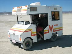 an ice cream truck is parked in the middle of the desert with two people inside