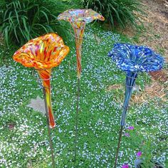 three colorful glass flowers are in the grass