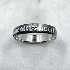 The Memento Mori Ring is not just a piece of jewellery; it is a talisman of empowerment and introspection. By wearing this ring, you carry a symbol of your own mortality, inviting reflection and inspiring a deeper appreciation for the fleeting beauty of life. It serves as a reminder to live fully, embracing the joys and challenges that come your way. Memento mori is a Latin phrase meaning 'remember you must die' Ring is 6mm wide. 925 Sterling Silver. Each piece is handmade to order in our Jewel Gothic Engraved Rings For Gift, Spiritual Promise Rings With Engraving Option, Symbolic Etched Jewelry For Promise, Symbolic Sterling Silver Engraved Ring, Symbolic Engraved Skull Ring Gift, Symbolic Engraved Skull Ring For Gift, Symbolic Engraved White Gold Skull Ring, Symbolic Engraved Ring With Oxidized Finish For Promises, Gothic Engraved Ring Jewelry