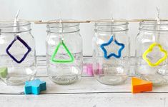 four mason jars with colored crayons in them on a white wooden table next to colorful erasers