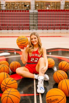 a woman sitting on the floor with basketballs in front of her and smiling at the camera