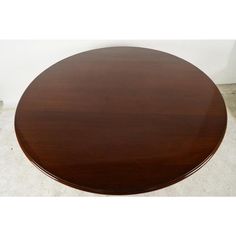 a round wooden table sitting on top of a tile floor next to a white wall