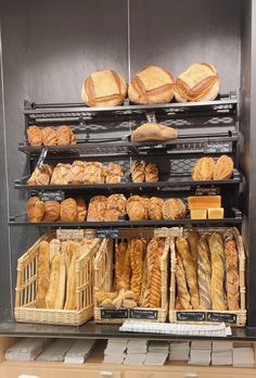 breads and pastries are on display in a bakery case with black shelves behind them