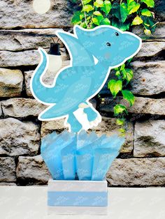 a paper cut out of a dolphin on top of some blue plastic bags in front of a stone wall