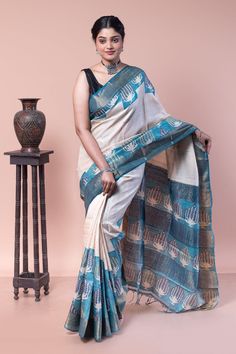 The floral buta is printed asymmetrically on this zari border saree, creating an illusion of steps. This saree is a classic example of a traditional block print represented in a modern way. COLOUR : Blue and white CRAFT : Hand block printing DIMENSIONS : Saree length 6.5 Mts., Saree width 1.14 Mts. Blouse piece inclusive. PATTERN : Floral buta Printing PRODUCT MATERIAL : Handwoven Pure Zari Border Tussar saree PRODUCT TYPE : Saree with Blouse piece WEIGHT : 450 g WASH INSTRUCTIONS : Dry Clean recommended for this product. Iron inside out. Do not bleach and expose this product to excessive heat and sunlight for long. Festive Tussar Silk Pre-draped Saree With Printed Border, Art Silk Pre-draped Saree With Printed Border, Semi-stitched Cotton Silk Saree With Printed Border, Block Print Tussar Silk Saree, Tussar Silk Saree Blouse Piece With Printed Border, Tussar Silk Saree With Printed Border, White Tussar Silk Saree With Block Print, Festive Block Print Saree For Transitional Season, Semi-stitched White Saree With Block Print