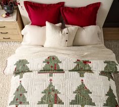 a white bed with red pillows and christmas trees on the comforter in front of it