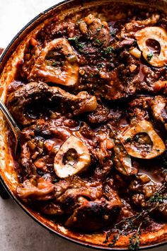 a skillet filled with meat and mushrooms covered in sauce, garnished with parsley