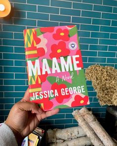 a person holding up a book in front of a blue brick wall with flowers on it