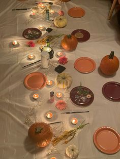 the table is set with candles, plates and pumpkins