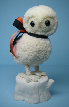 a white stuffed animal sitting on top of a wooden stump with an orange ribbon around it's neck