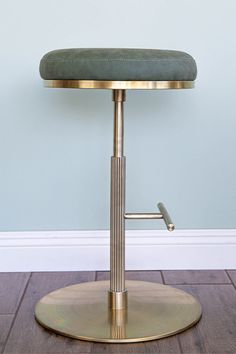 a gold metal stool with a green cushion on the back and foot rests in front of a blue wall