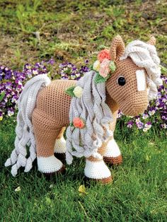 a crocheted horse is standing in the grass with flowers on it's head