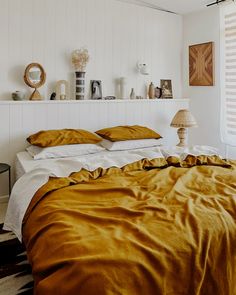 a bed with gold sheets and pillows in a white room next to a wall mounted shelf