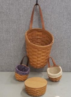 three baskets with handles hanging on a wall next to two small bowls and one larger basket