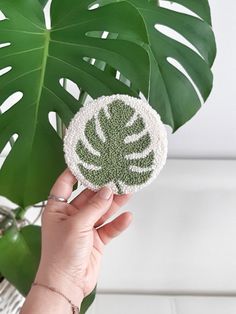 a person holding up a green and white brooch on top of a palm leaf