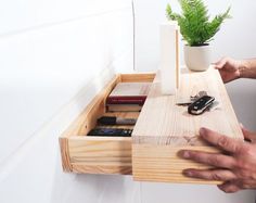 a person holding a wooden drawer with keys and other items in it, next to a potted plant