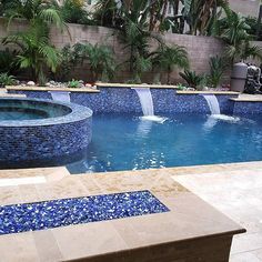 an outdoor swimming pool surrounded by palm trees and blue glass mosaic tiles with waterfalls