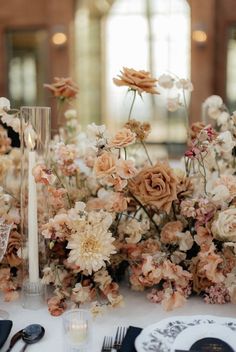 an arrangement of flowers on a table with candles and place settings in front of them