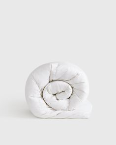 a white comforter on a grey background with the top half rolled up to look like a spiral