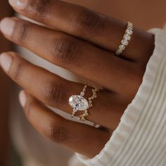 a woman's hand wearing a diamond ring and gold band with an oval shaped diamond on it