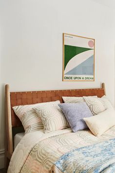 a bed with pillows and blankets on top of it next to a painting hanging above the headboard