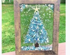 a wooden frame with a glass christmas tree in the center and sea shells around it