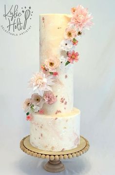 a three tiered white cake with pink flowers on the top and bottom, sitting on a wooden stand