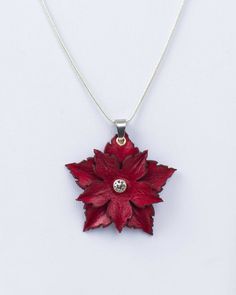 a red flower is hanging from a silver chain on a white surface with a diamond in the center